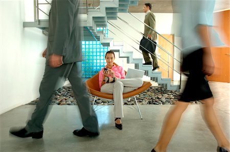 Femme d'affaires assis sur une chaise avec ordinateur portable tout en marchant sur le plancher des collègues Photographie de stock - Premium Libres de Droits, Code: 6108-05859343