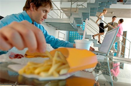 fast food photographs - Young businessman using laptop and eating French fries Stock Photo - Premium Royalty-Free, Code: 6108-05859350