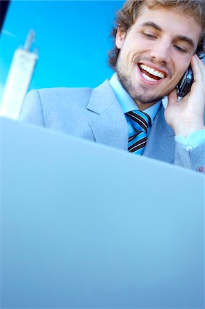 simsearch:6108-05859384,k - Young businessman using mobile phone and laptop, smiling Stock Photo - Premium Royalty-Free, Code: 6108-05859387