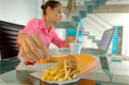 food and fast food - Businesswoman eating French fries, using laptop Stock Photo - Premium Royalty-Free, Code: 6108-05859328