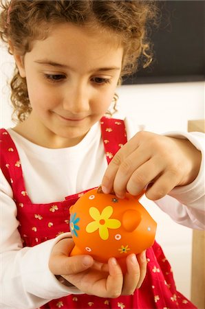 Girl putting a coin into a piggy bank Stock Photo - Premium Royalty-Free, Code: 6108-05860250