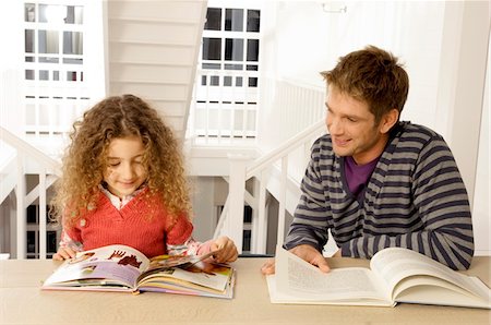 Mid adult man sitting with his daughter and reading books Stock Photo - Premium Royalty-Free, Code: 6108-05860290