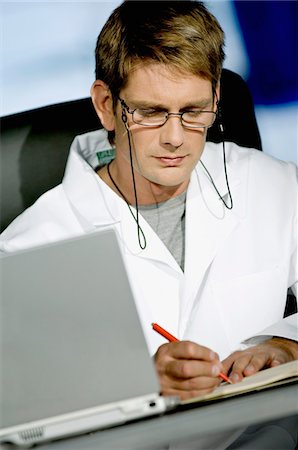 Male doctor sitting at a desk in his office and writing in a notebook Stock Photo - Premium Royalty-Free, Code: 6108-05860376