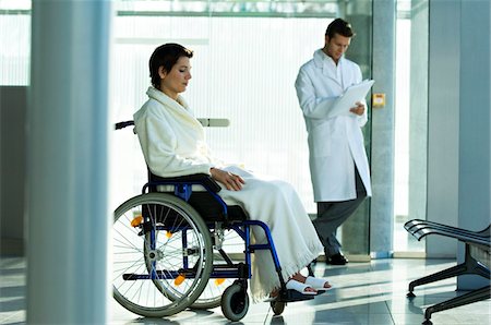 simsearch:6108-05860422,k - Patient féminin, assis dans un fauteuil roulant et un médecin de sexe masculin debout en arrière-plan Photographie de stock - Premium Libres de Droits, Code: 6108-05860418