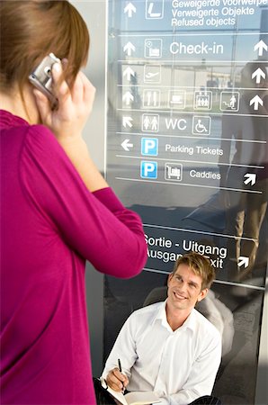 pictures of two people talking at the airport - Businesswoman talking on a mobile phone with a businessman sitting in front of her Stock Photo - Premium Royalty-Free, Code: 6108-05860547