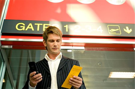 passenger at airport - Low angle view of a businessman holding a boarding pass and using a mobile phone Stock Photo - Premium Royalty-Free, Code: 6108-05860548