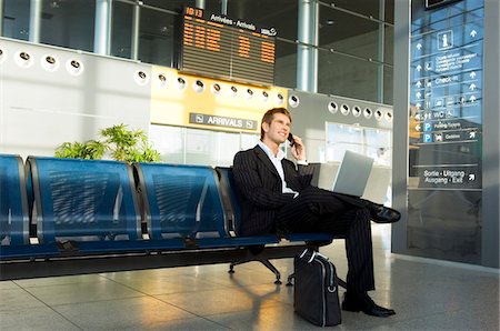 Businessman using a laptop and talking on a mobile phone at an airport lounge Stock Photo - Premium Royalty-Free, Code: 6108-05860582