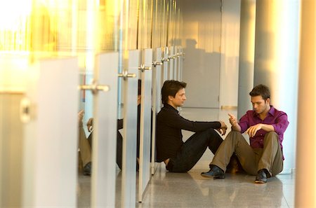 Two businessmen sitting in a corridor and talking with each other Stock Photo - Premium Royalty-Free, Code: 6108-05860518
