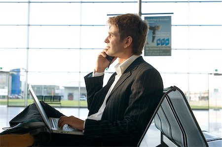 position assise en tailleur - Profil de côté d'un homme d'affaires à l'aide d'un ordinateur portable et de parler sur un téléphone mobile à un salon de l'aéroport Photographie de stock - Premium Libres de Droits, Code: 6108-05860535