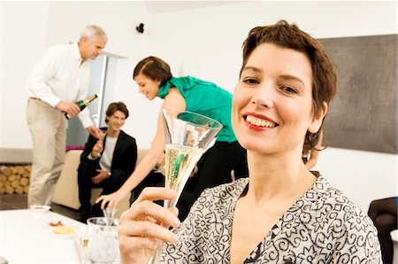 party room - Mid adult woman holding a wine glass with three people in the background Stock Photo - Premium Royalty-Free, Code: 6108-05860609
