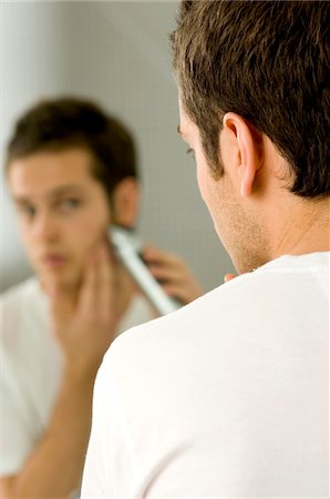 Rear view of a young man shaving with an electric razor Stock Photo - Premium Royalty-Free, Code: 6108-05860767