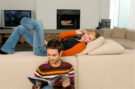 Young man reading a magazine with a young woman using a mobile phone behind him Foto de stock - Sin royalties Premium, Código: 6108-05860728