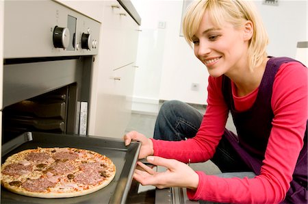 Young woman putting a tray of pizza into an oven Stock Photo - Premium Royalty-Free, Code: 6108-05860820
