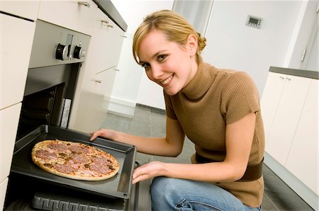 Portrait of a young woman putting a tray of pizza into an oven Stock Photo - Premium Royalty-Free, Code: 6108-05860836