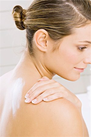 Side profile of a young woman applying moisturizer on her shoulder Foto de stock - Sin royalties Premium, Código: 6108-05860941