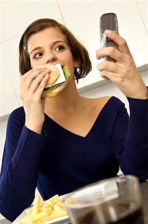 french fry smile - Close-up of a young woman eating a burger and looking at a mobile phone Stock Photo - Premium Royalty-Free, Code: 6108-05861029