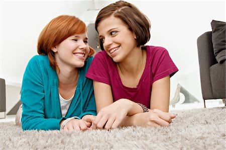 Close-up of two young women lying on a carpet and smiling Stock Photo - Premium Royalty-Free, Code: 6108-05861175