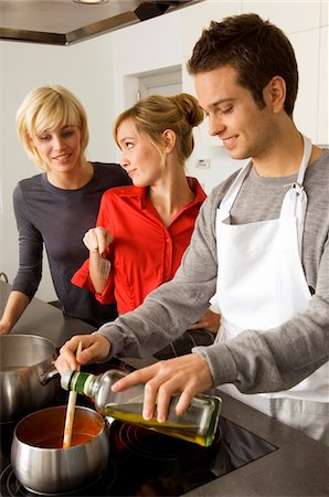 Two young women and a young man preparing food in the kitchen Stock Photo - Premium Royalty-Free, Code: 6108-05861105