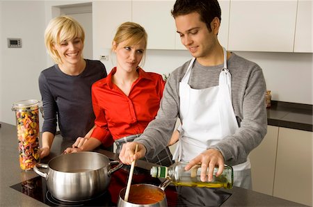 sauce in ladel - Two young women and a young man preparing food in the kitchen Stock Photo - Premium Royalty-Free, Code: 6108-05861119