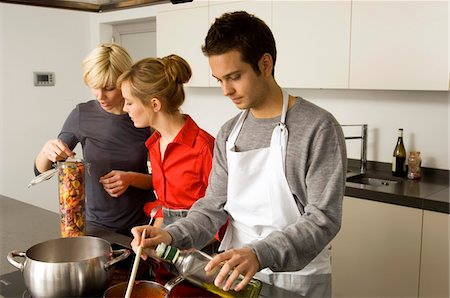 sauce in ladel - Two young women and a young man preparing food in the kitchen Stock Photo - Premium Royalty-Free, Code: 6108-05861123