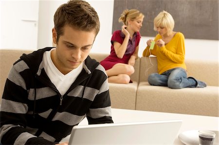 simsearch:6108-05860003,k - Young man using a laptop with two young women listening to an MP3 player in the background Stock Photo - Premium Royalty-Free, Code: 6108-05861126