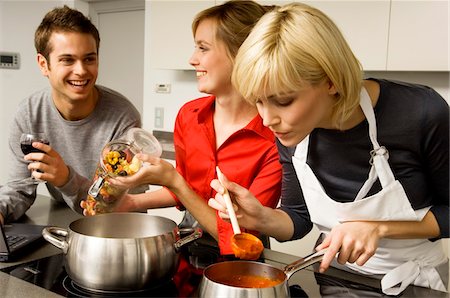 simsearch:6108-05874120,k - Deux jeunes femmes et un jeune homme, préparation de la nourriture dans la cuisine Photographie de stock - Premium Libres de Droits, Code: 6108-05861130