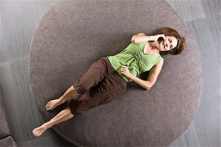 Woman lying on a round sofa and talking on a mobile phone Stock Photo - Premium Royalty-Free, Code: 6108-05862184