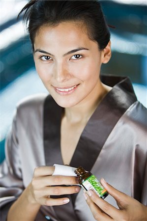 Woman holding a bottle of aromatherapy oil and smiling Stock Photo - Premium Royalty-Free, Code: 6108-05862220