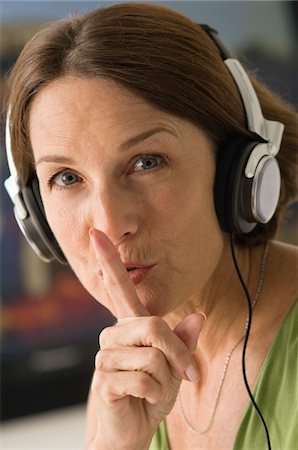 Femme à l'écoute au casque avec son doigt sur ses lèvres Photographie de stock - Premium Libres de Droits, Code: 6108-05862324