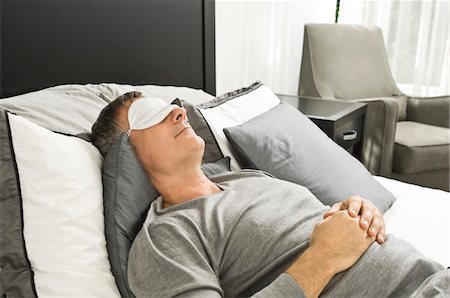 Man sleeping in bed wearing an eye mask Stock Photo - Premium Royalty-Free, Code: 6108-05862586