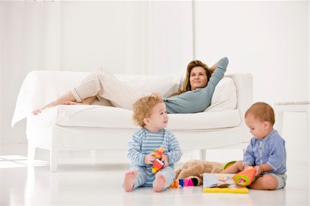 Enfants jouant avec des jouets et leur mère reposant sur un canapé Photographie de stock - Premium Libres de Droits, Code: 6108-05863183