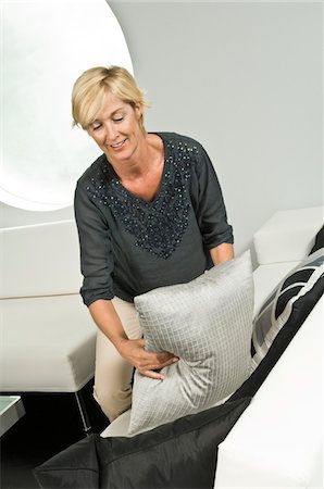 simsearch:6108-05856445,k - Woman arranging cushions on a couch and smiling Fotografie stock - Premium Royalty-Free, Codice: 6108-05863319