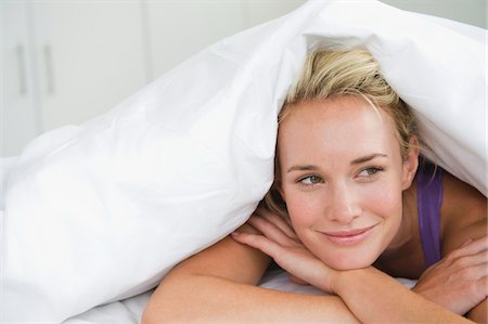 duvet - Close-up of a woman lying on the bed and smiling Stock Photo - Premium Royalty-Free, Code: 6108-05864286
