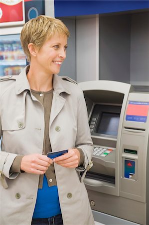 Woman holding a credit card and standing in front of an ATM Stock Photo - Premium Royalty-Free, Code: 6108-05864539