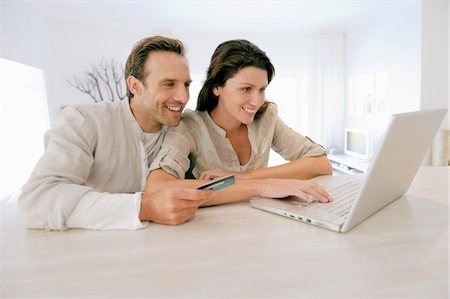 smiling brunette man looking at laptop - Couple holding a credit card and working on a laptop Stock Photo - Premium Royalty-Free, Code: 6108-05864691