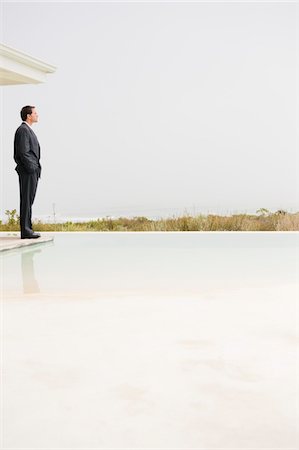 Businessman standing at the poolside and looking at sea view Stock Photo - Premium Royalty-Free, Code: 6108-05865027