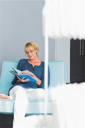 simsearch:6108-05856799,k - Femme lisant un livre sur un canapé Photographie de stock - Premium Libres de Droits, Code: 6108-05865374