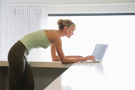 simsearch:6108-05859712,k - Woman leaning on a counter and working on a laptop Foto de stock - Royalty Free Premium, Número: 6108-05865746