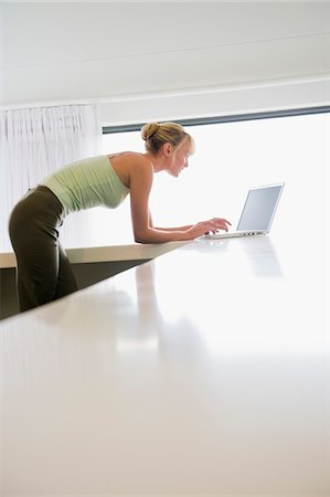 simsearch:6108-05859712,k - Woman leaning on a counter and working on a laptop Foto de stock - Royalty Free Premium, Número: 6108-05865751