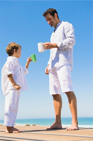 Man and his son holding coffee cups on the beach Stock Photo - Premium Royalty-Free, Code: 6108-05865860