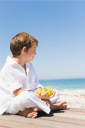 Boy sitting on a boardwalk and holding grapes Foto de stock - Sin royalties Premium, Código: 6108-05865957