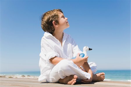 Boy sitting on a boardwalk and holding a toy bird Stock Photo - Premium Royalty-Free, Code: 6108-05865922