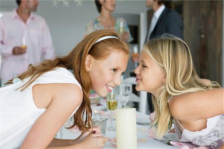 Girl whispering to her sister across a dining table Stock Photo - Premium Royalty-Free, Code: 6108-05866256
