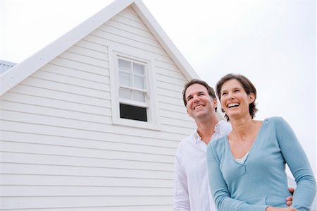 real estate people eye contact - Couple smiling with a house in the background Stock Photo - Premium Royalty-Free, Code: 6108-05866711