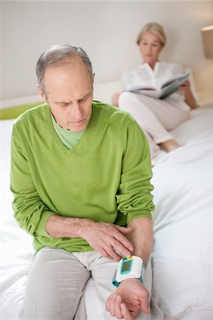 senior blood pressure - Man checking his blood pressure with a woman in the background Foto de stock - Sin royalties Premium, Código: 6108-05867275