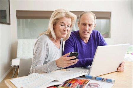 senior couple table - Woman text messaging on a mobile phone with her husband sitting beside her Stock Photo - Premium Royalty-Free, Code: 6108-05867360