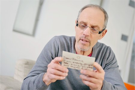 postcard - Man looking serious while reading a postcard Stock Photo - Premium Royalty-Free, Code: 6108-05867476