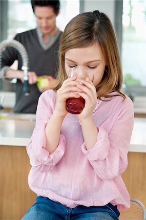 Girl drinking juice with her father standing behind her Stock Photo - Premium Royalty-Free, Code: 6108-05867492