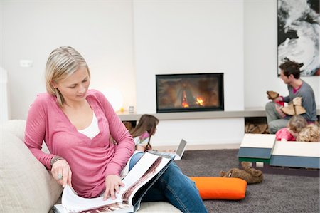foyer (âtre) - Femme lisant un magazine avec sa famille dans une salle de séjour Photographie de stock - Premium Libres de Droits, Code: 6108-05867672