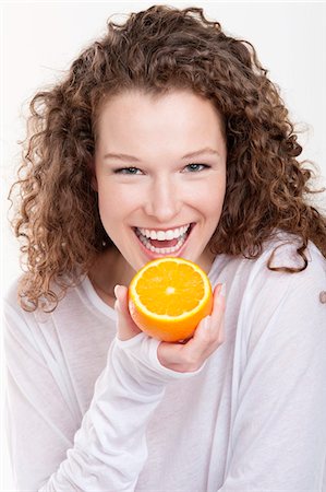 Portrait of a woman holding a half of an orange and laughing Stock Photo - Premium Royalty-Free, Code: 6108-05867852
